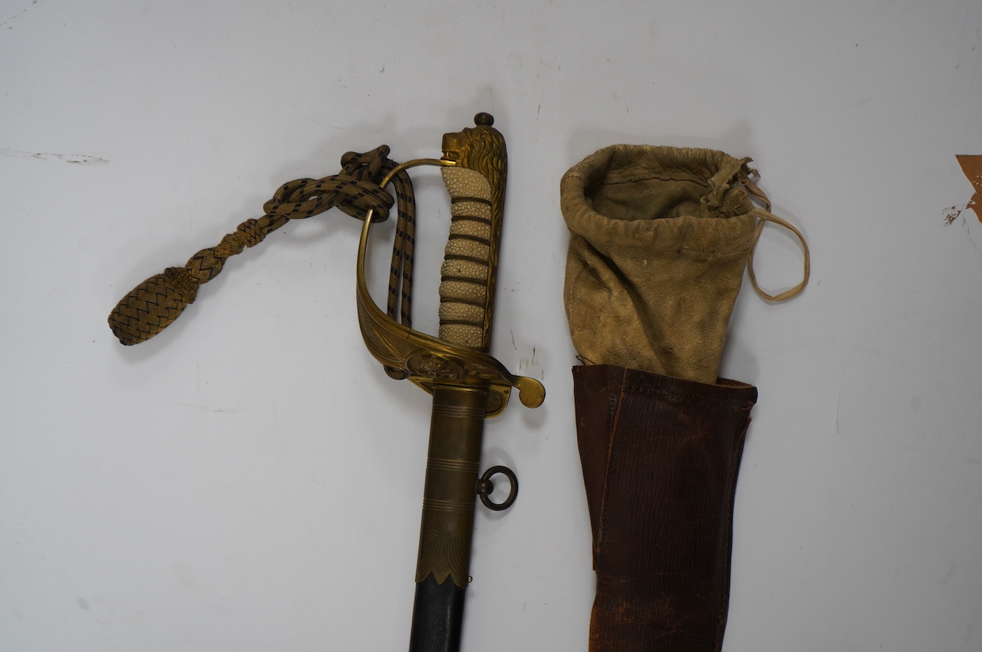 A George VI naval officer’s dress sword by Wilkinson (unnumbered), with regulation brass hilt with folding guard, engraved P.A.R. Gould R.N., bullion dress knot, in its brass mounted leather scabbard and contained in its